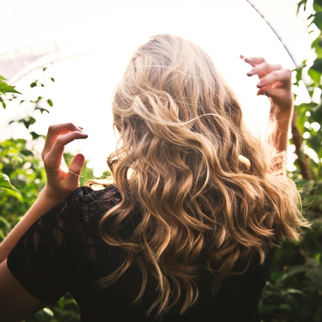 Blonde woman with curly hair surrounded by lush greenery, enjoying a sunny day.