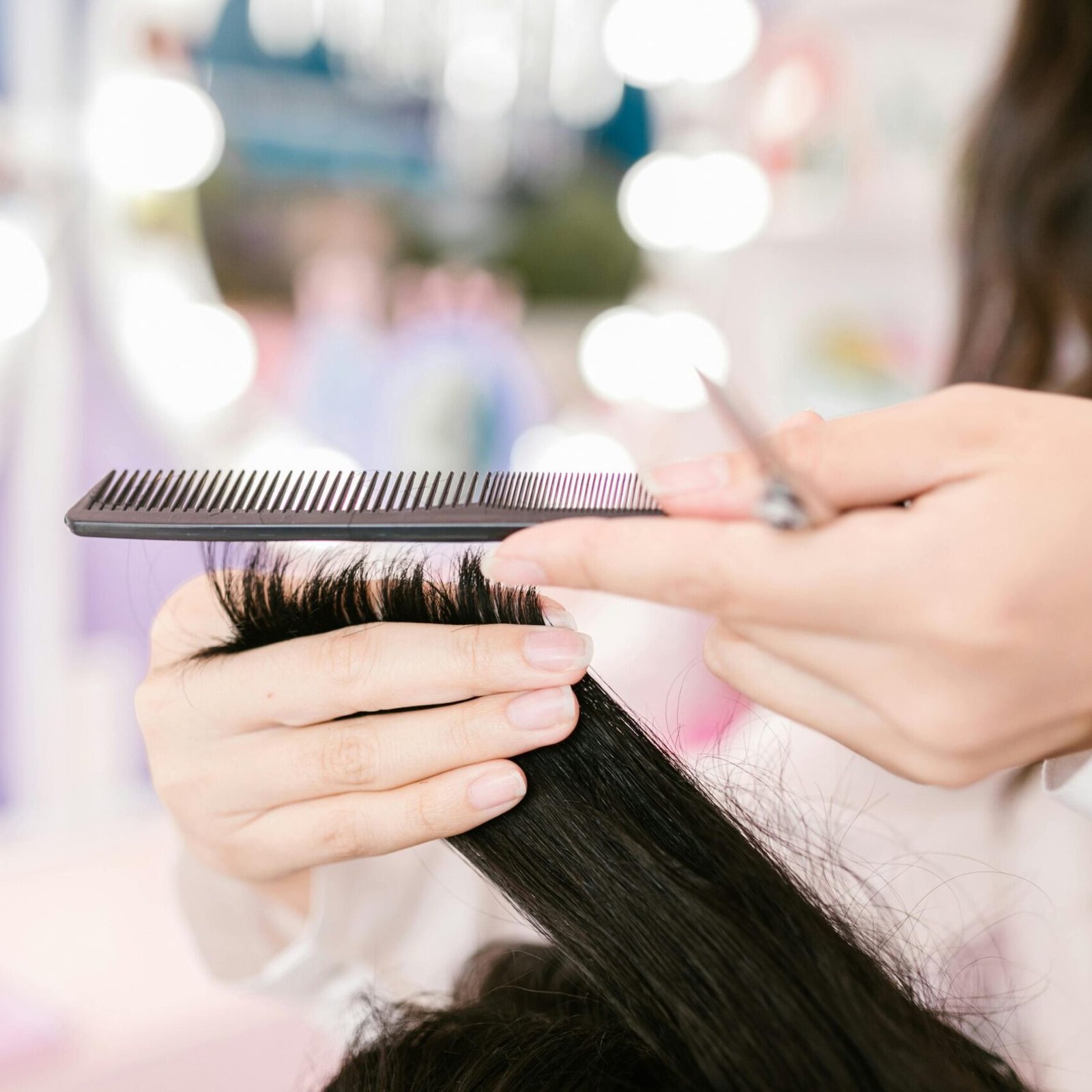 Close-up of a hairdresser grooming hair with scissors and a comb in a salon setting.